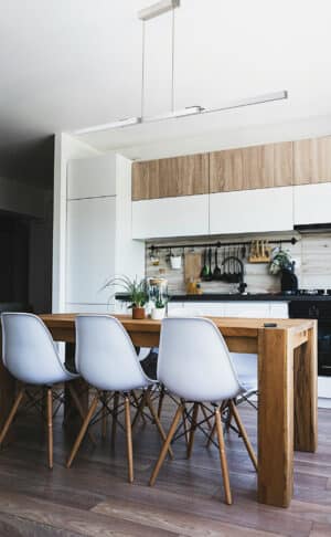 Abiant image of an expandable linear pendant in a kitchen above a wooden dining room table with white dining room chairs
